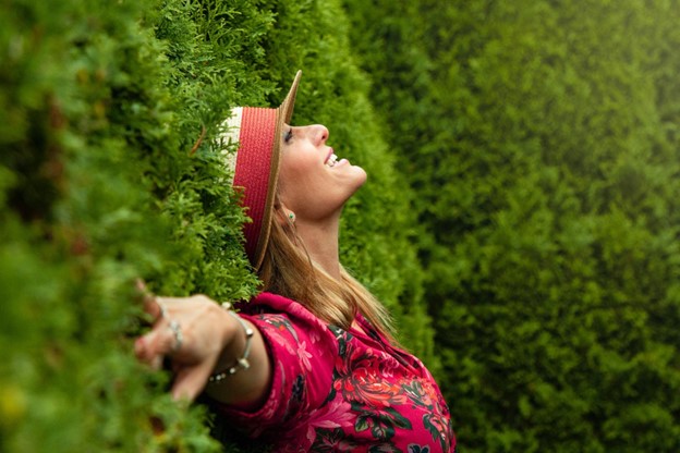 A girl leaning against bushes, smiling with arms spread out wide